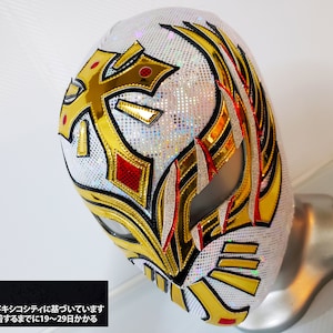 May include: White wrestling mask with gold and red accents. The mask features a cross design and a wing pattern. The text "警告" is visible on the mask.