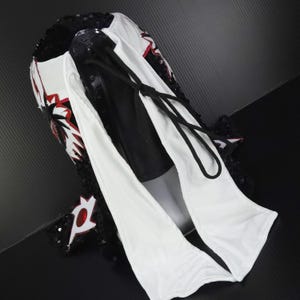 Puede incluir: Una m&aacute;scara de lucha libre profesional con un dise&ntilde;o blanco, negro y rojo. La m&aacute;scara presenta un ribete de lentejuelas negras, detalles rojos y un cord&oacute;n negro. La m&aacute;scara est&aacute; hecha de una combinaci&oacute;n de materiales.