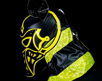 May include: A black and yellow wrestling mask with a skull and horns design. The mask is made of a shiny material and has a textured surface.
