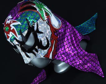 Puede incluir: Una máscara de lucha libre con un diseño morado, verde y blanco. La máscara presenta un dragón con escamas y una cara en blanco y negro.