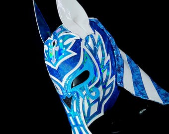 May include: A blue and white wrestling mask with a white pointed ear on the left side. The mask has a blue and white design with a white ankh symbol on the forehead.
