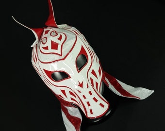 May include: A white wrestling mask with red accents and a stylized design. The mask has two long, pointed horns on top and a white and red fringe around the bottom.