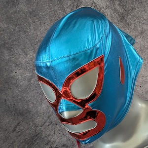 May include: A shiny blue wrestling mask with red detailing. The mask has a metallic sheen and a traditional design with eye and mouth cutouts. A red teardrop shape is on the side. This mask is likely for costume or performance use.