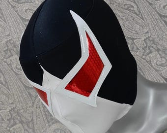 Peut inclure: Un masque de lutte noir et blanc avec un motif rouge en forme de diamant sur le devant. Le masque a un sommet pointu et une bordure blanche autour du motif rouge.