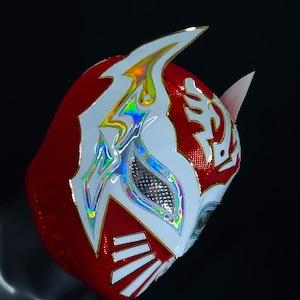 Op de afbeelding: Een rood en wit worstelmasker met een holografisch ontwerp. Het masker heeft een witte hoorn aan de bovenkant en een wit ontwerp aan de zijkant. Het masker is gemaakt van een glanzend materiaal.