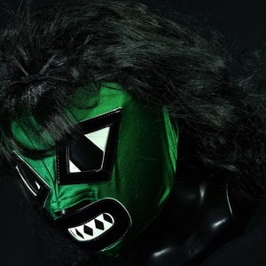 May include: Green lucha libre wrestling mask with black and white details. The mask has a fierce expression with a large mouth and sharp teeth.