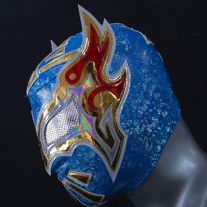 Op de afbeelding: Een blauw worstelmasker met een gouden en wit ontwerp. Het masker heeft een rood en wit vlammenontwerp aan de bovenkant.