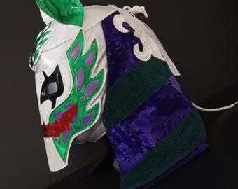 May include: A white and silver lucha libre mask with green, purple, and red accents. The mask features a stylized design with a green leaf-shaped element on top and a flowing, sequined purple and green section on the side.