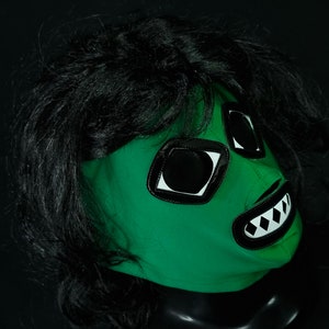 May include: Green wrestling mask with black hair, white and black eyes, and a white and black toothy grin.