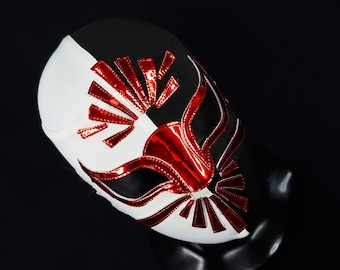 Puede incluir: Una máscara de lucha libre negra y blanca con detalles rojos. La máscara tiene un diseño estilizado con un patrón geométrico rojo brillante.