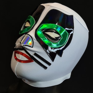 Puede incluir: Máscara de lucha libre blanca con detalles negros, verdes e iridiscentes. La máscara presenta un diseño felino con una nariz negra, labios rojos y dos rayas negras.