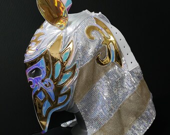 May include: A professional wrestling mask with a white base, adorned with gold and iridescent accents. The mask features a detailed design with blue and gold leaf-like patterns, and a sequined cape. The mask has a gold ear-like shape on top.
