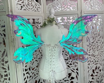 May include: A pair of iridescent blue and green fairy wings with a glittery finish. The wings are attached to a white corset.