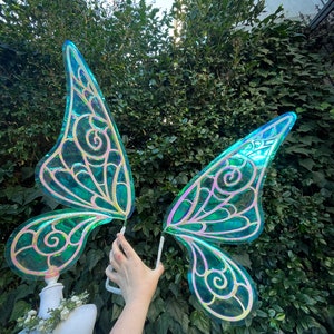 May include: A pair of iridescent green fairy wings with gold detailing. The wings are made of a translucent material and have a delicate, whimsical design.