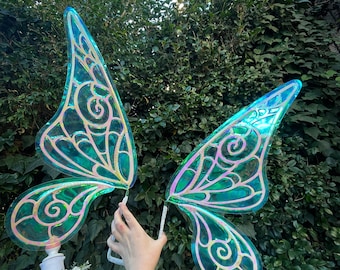 May include: A pair of iridescent green fairy wings with gold detailing. The wings are made of a translucent material and have a delicate, whimsical design.