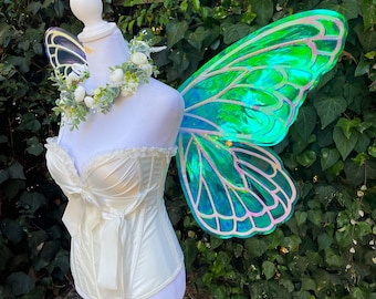 May include: A white satin corset with a bow and lace trim, paired with a green iridescent butterfly fairy wings costume.