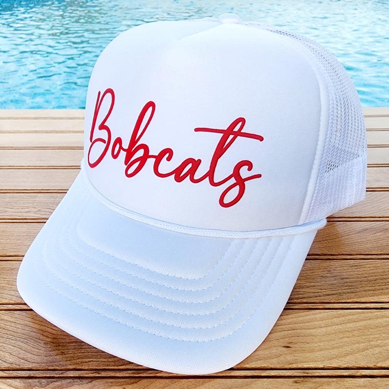 以下が含まれることがあります： 赤い刺繍の「Bobcats」ロゴが付いた白いトラッカーハット。帽子はメッシュバックと白いフロントです。