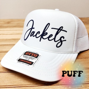 May include: White trucker hat with a black mesh back and a navy blue "Jackets" logo. The hat has a black and red label that reads "OTTO World Famous Foam Front OSFM Trucker Durable Snap Closure".