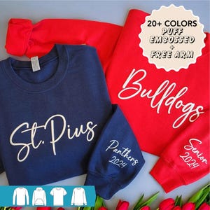 May include: Two sweatshirts, one navy blue and one red, with white puff embossed lettering. The navy blue sweatshirt says "St. Pius" and "Panthers 2024". The red sweatshirt says "Bulldogs" and "Senior 2024".