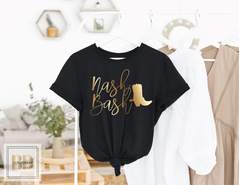 Op de afbeelding: Zwart T-shirt met gouden lettertype dat "Nash Bash" zegt en een gouden silhouet van een cowboylaars.