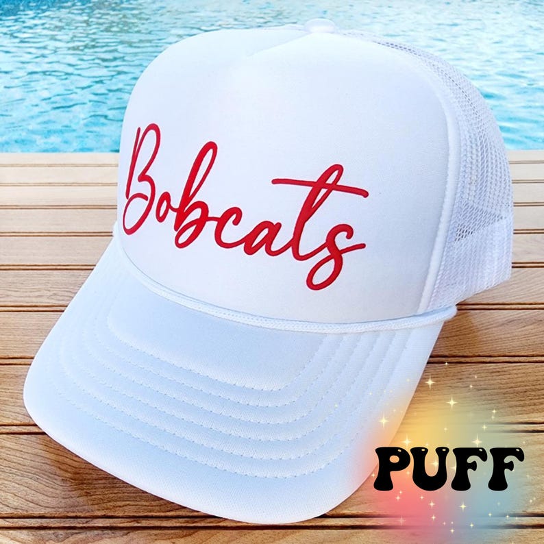 May include: White trucker hat with a red embroidered "Bobcats" logo. The hat has a mesh back and a white front panel.