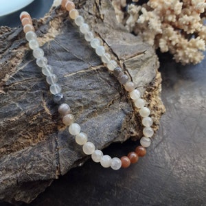 May include: A multi-colored beaded necklace with shades of brown, gray, and white. The beads are round and smooth, and the necklace is strung on a clear cord.