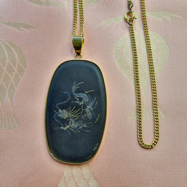 May include: A gold chain necklace with a black oval pendant featuring a white dragon design.
