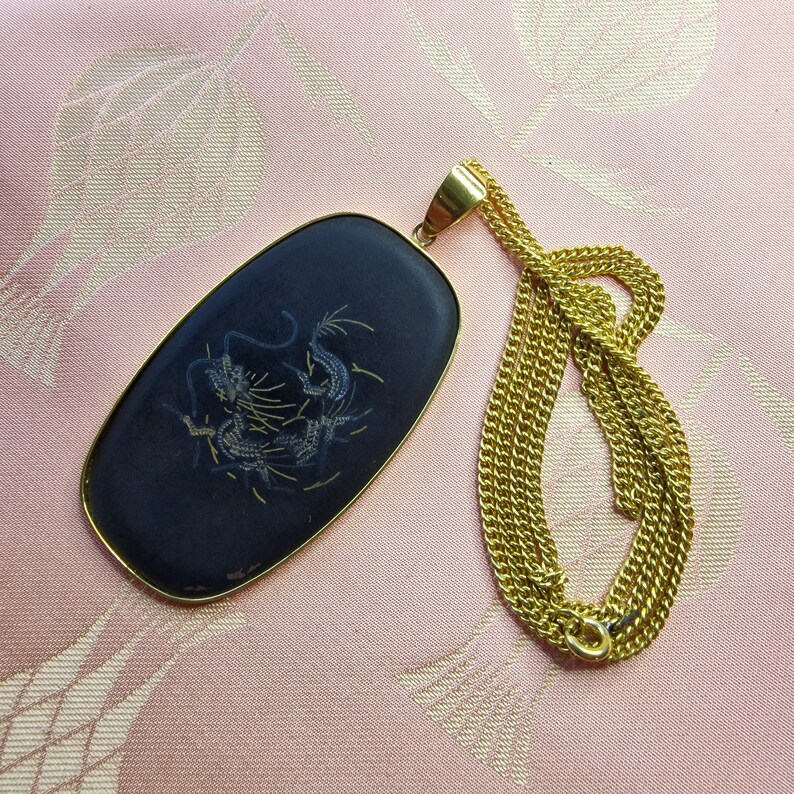 May include: A gold chain necklace with a black oval pendant featuring a gold dragon design.
