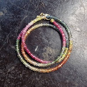 May include: A multi-colored gemstone necklace with a gold clasp. The necklace is made of small, faceted gemstones in shades of pink, yellow, green, and blue.