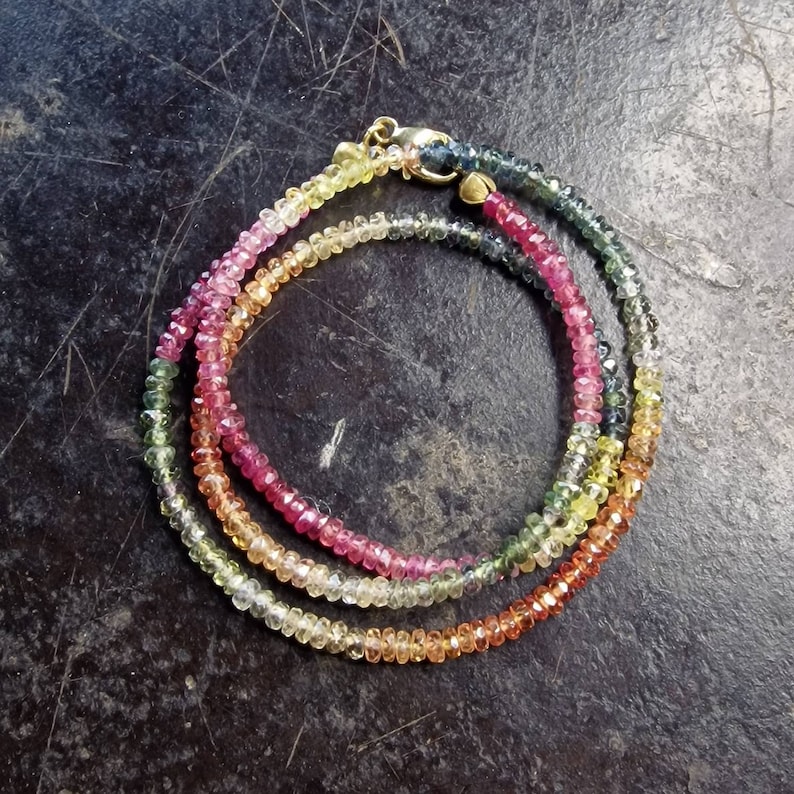 May include: A multi-colored gemstone necklace with a gold clasp. The necklace is made of small, faceted gemstones in shades of pink, yellow, green, and blue.