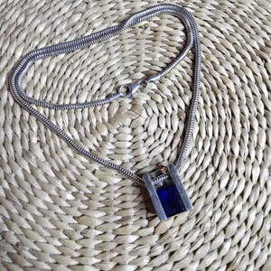 May include: A silver chain necklace with a rectangular pendant featuring a dark blue gemstone.