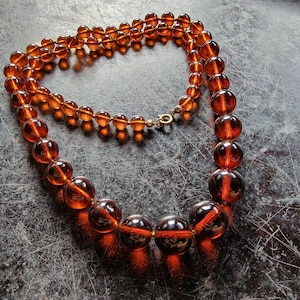 May include: A long amber glass bead necklace with a gold clasp. The beads are round and have a smooth, polished finish.