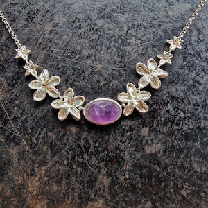 May include: A silver necklace with a purple gemstone pendant and flower-shaped charms.