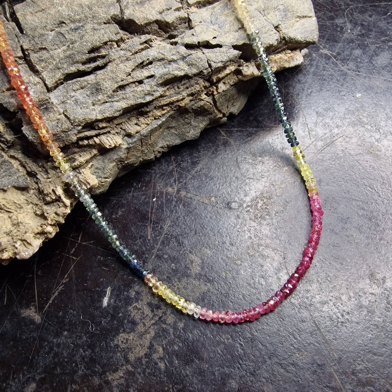 May include: A rainbow sapphire gemstone necklace with faceted beads in shades of red, pink, yellow, green, blue, and black.