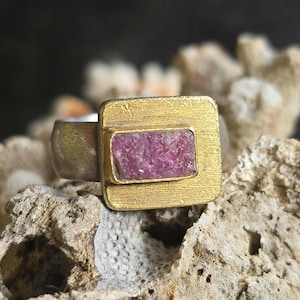 Puede incluir: Un anillo de plata con un engaste cuadrado de oro que presenta una piedra preciosa rosa en bruto.