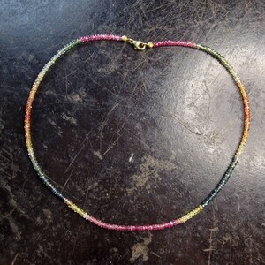 May include: A multi-colored gemstone necklace with a gold clasp. The necklace is made of small, round beads in shades of pink, yellow, green, and blue.