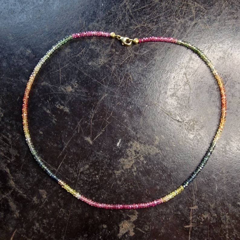 May include: A multi-colored gemstone necklace with a gold clasp. The necklace is made of small, round beads in shades of pink, yellow, green, and blue.