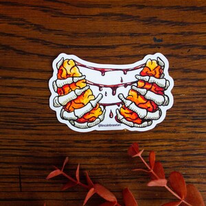 May include: A sticker featuring a pair of orange and white brains with dripping red blood, surrounded by a white background. The sticker has the text "@lincolnbraseart" at the bottom.