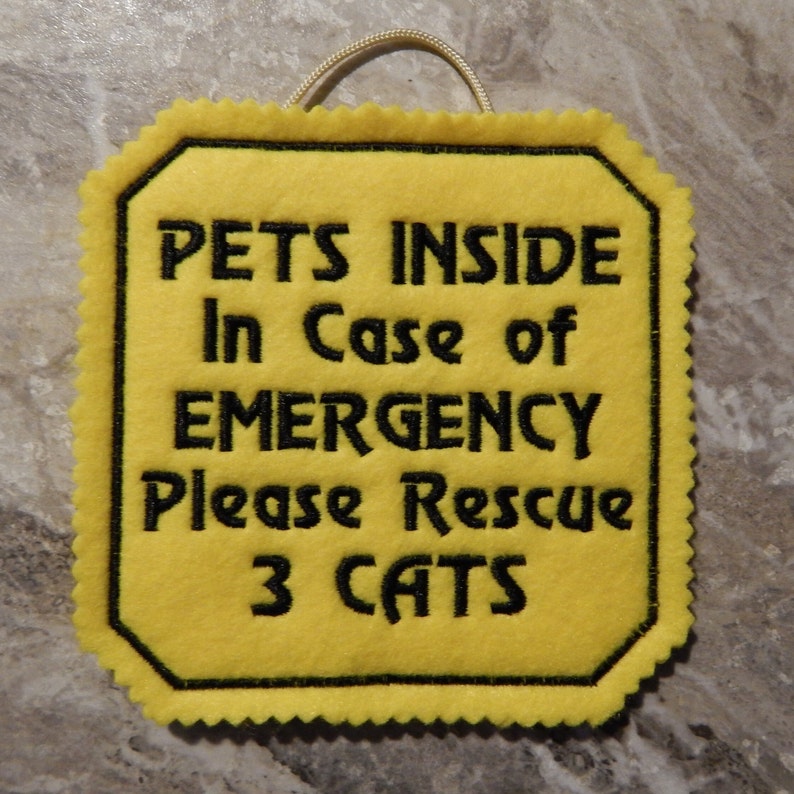 Bright yellow felt sign embroidered with PETS INSIDE In case of EMERGENCY Please Rescue 3 CATS in bold letters with black thread. 
Has yellow felt on the back with paracord for hanging. Edges are done with pinking shears. Size approx. 5x5 square