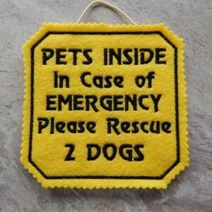 Bright yellow felt sign embroidered with PETS INSIDE In case of EMERGENCY Please Rescue 2 DOGS in bold letters with black thread. 
Has yellow felt on the back with paracord for hanging. Edges are done with pinking shears. Size approx. 5x5 square