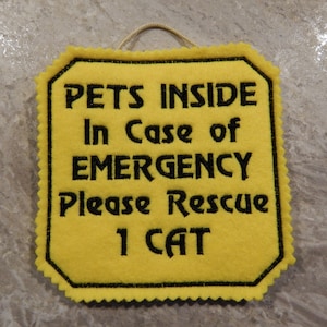 Bright yellow felt sign embroidered with PETS INSIDE In case of EMERGENCY Please Rescue 1 CAT in bold letters with black thread. 
Has yellow felt on the back with paracord for hanging. Edges are done with pinking shears. Size approx. 5x5 square