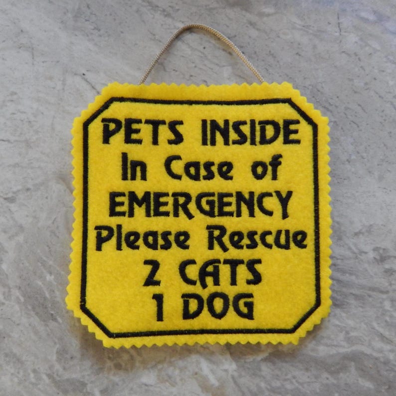 May include: A yellow felt sign with scalloped edges and a hanging string. The sign features black embroidered text that reads: PETS INSIDE In Case of EMERGENCY Please Rescue 2 CATS 1 DOG. The sign has a black border around the text.