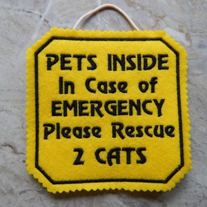Bright yellow felt sign embroidered with PETS INSIDE In case of EMERGENCY Please Rescue 2 CATS in bold letters with black thread. 
Has yellow felt on the back with paracord for hanging. Edges are done with pinking shears. Size approx. 5x5 square