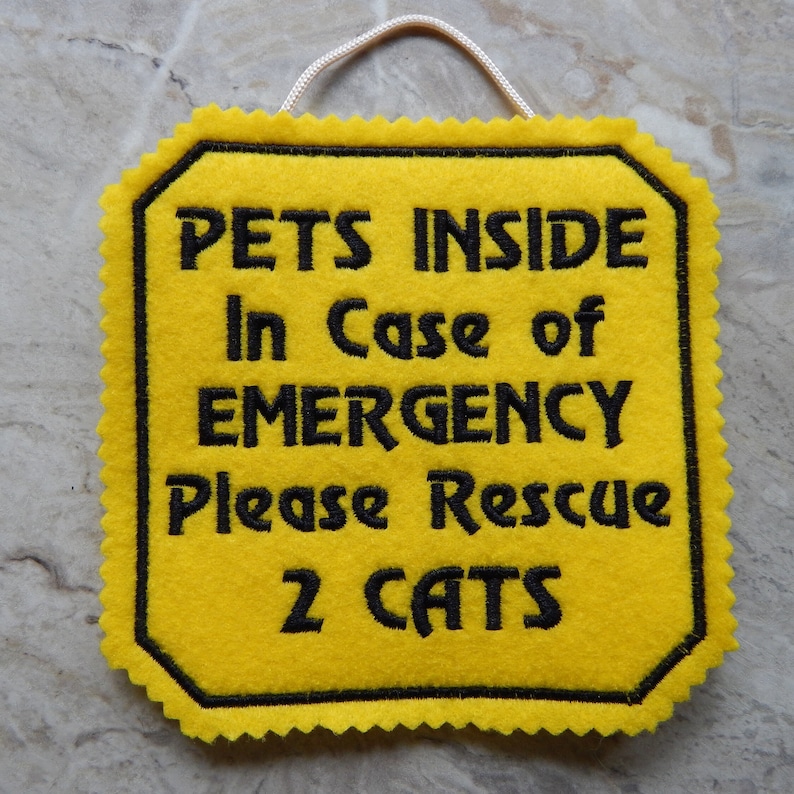 Bright yellow felt sign embroidered with PETS INSIDE In case of EMERGENCY Please Rescue 2 CATS in bold letters with black thread. 
Has yellow felt on the back with paracord for hanging. Edges are done with pinking shears. Size approx. 5x5 square