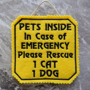 Bright yellow felt sign embroidered with PETS INSIDE In case of EMERGENCY Please Rescue 1 CAT 1 DOG in bold letters with black thread. 
Has yellow felt on the back with paracord for hanging. Edges are done with pinking shears. Size approx. 5x5 square