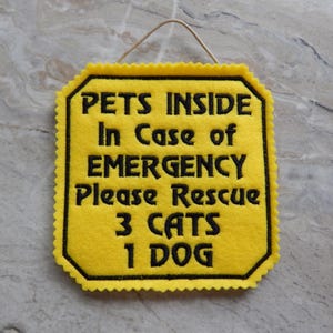 Bright yellow felt sign embroidered with PETS INSIDE In case of EMERGENCY Please Rescue 3 CATS 1 DOG in bold letters with black thread. 
Has yellow felt on the back with paracord for hanging. Edges are done with pinking shears. Size approx. 5x5 square.