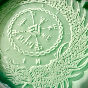 Può includere: Uno stampo circolare verde con un design rialzato di una bussola con un triangolo al centro e ali di drago su entrambi i lati.
