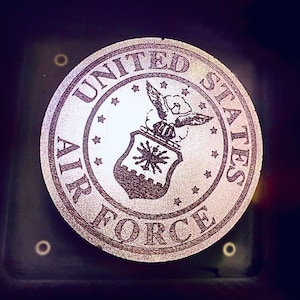 May include: A silver round emblem with the words "United States Air Force" in a circle around a stylised eagle and shield.