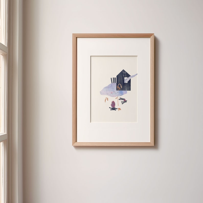May include: A framed art print featuring a collage-style illustration. The artwork depicts a dark blue house with a chimney, set against a light blue and purple background. The frame is made of light-colored wood.