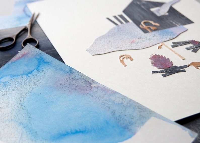 May include: An artistic composition featuring watercolor paper with blue and purple hues, alongside cut paper elements and a pair of scissors. The cutouts include abstract shapes and textures, suggesting a collage or mixed-media art project.
